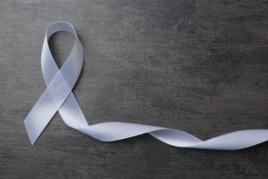 Photo of White awareness ribbon on grey table, top view. Space for text