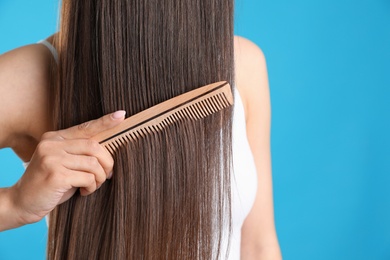 Photo of Young woman with wooden hair comb on color background, closeup. Space for text