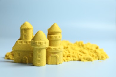 Castle figures made of yellow kinetic sand on light blue background, closeup. Space for text