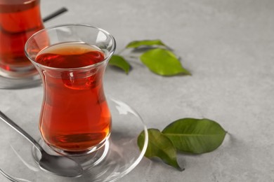 Glasses with traditional Turkish tea and green leaves on light grey table, closeup. Space for text