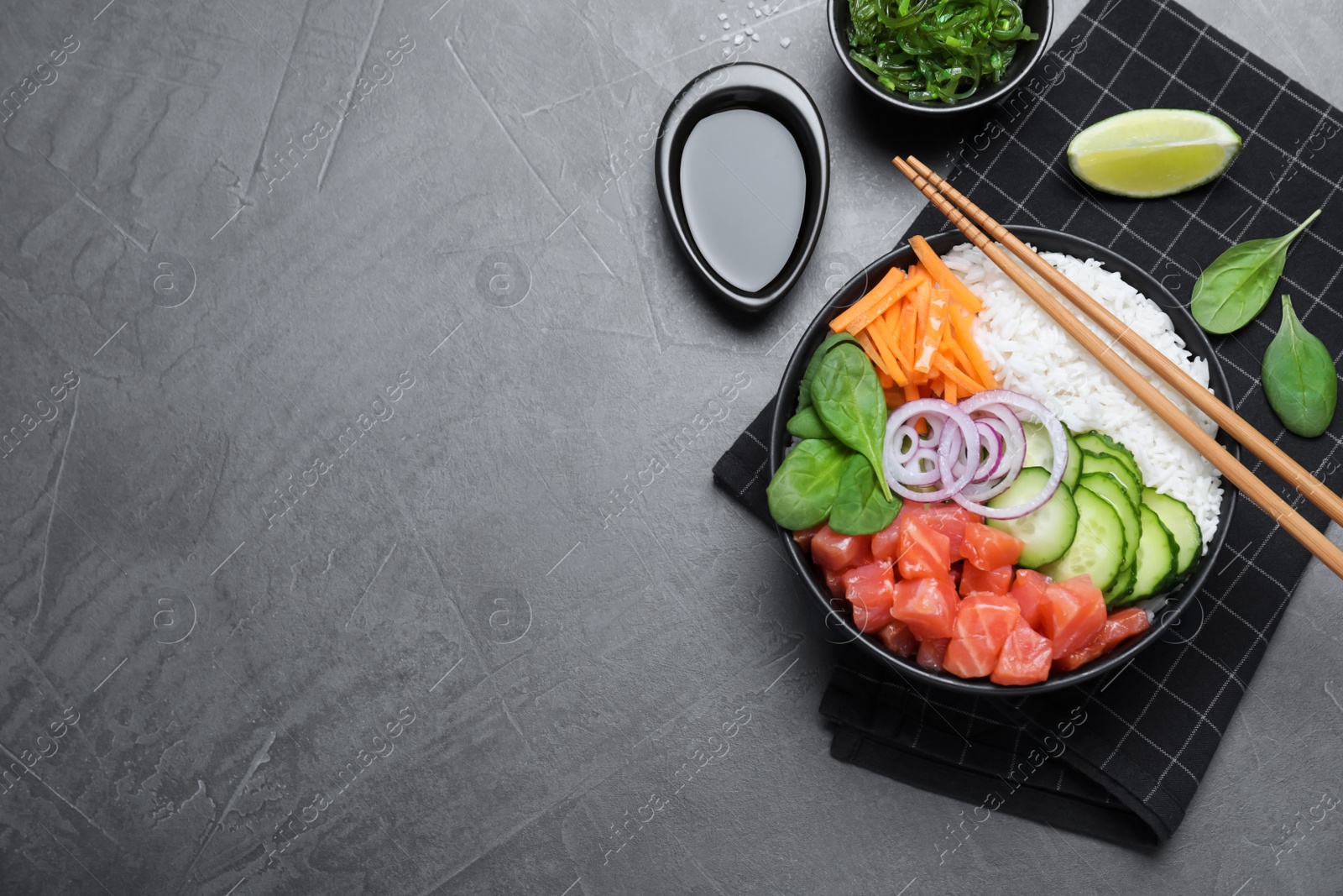 Photo of Delicious poke bowl with salmon and vegetables served on grey table, flat lay. Space for text