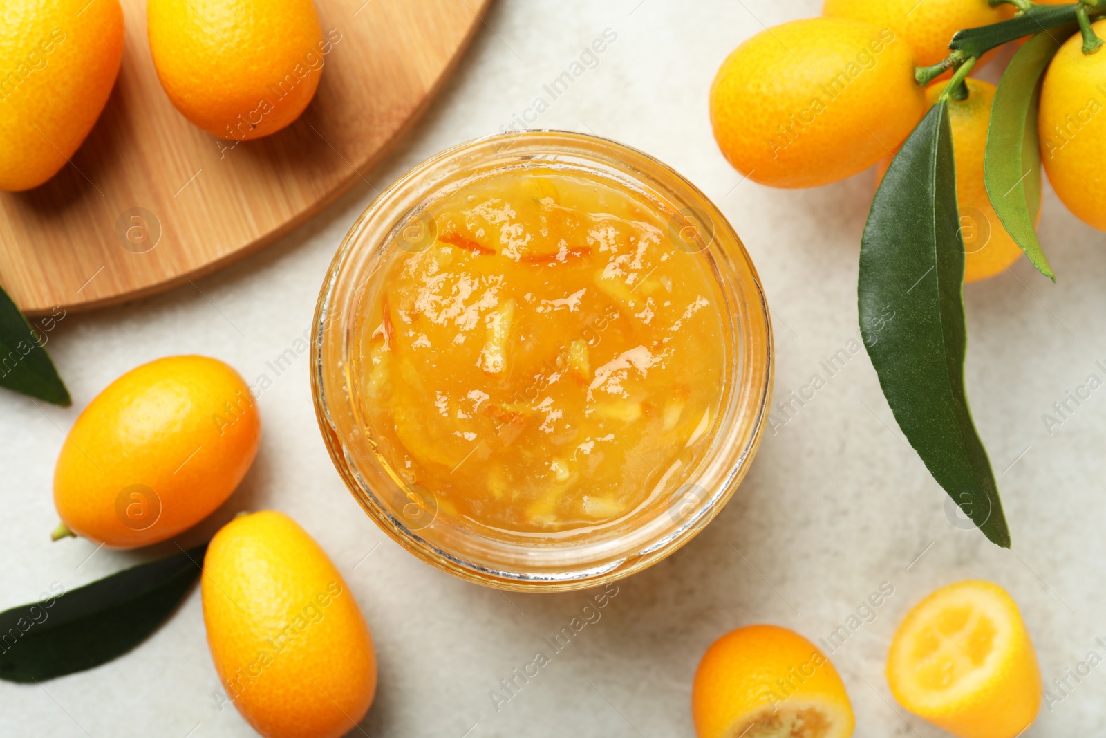 Photo of Delicious kumquat jam in jar and fresh fruits on light grey table, flat lay