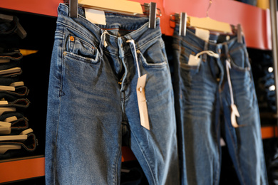 Photo of Modern jeans hanging on shelf in shop