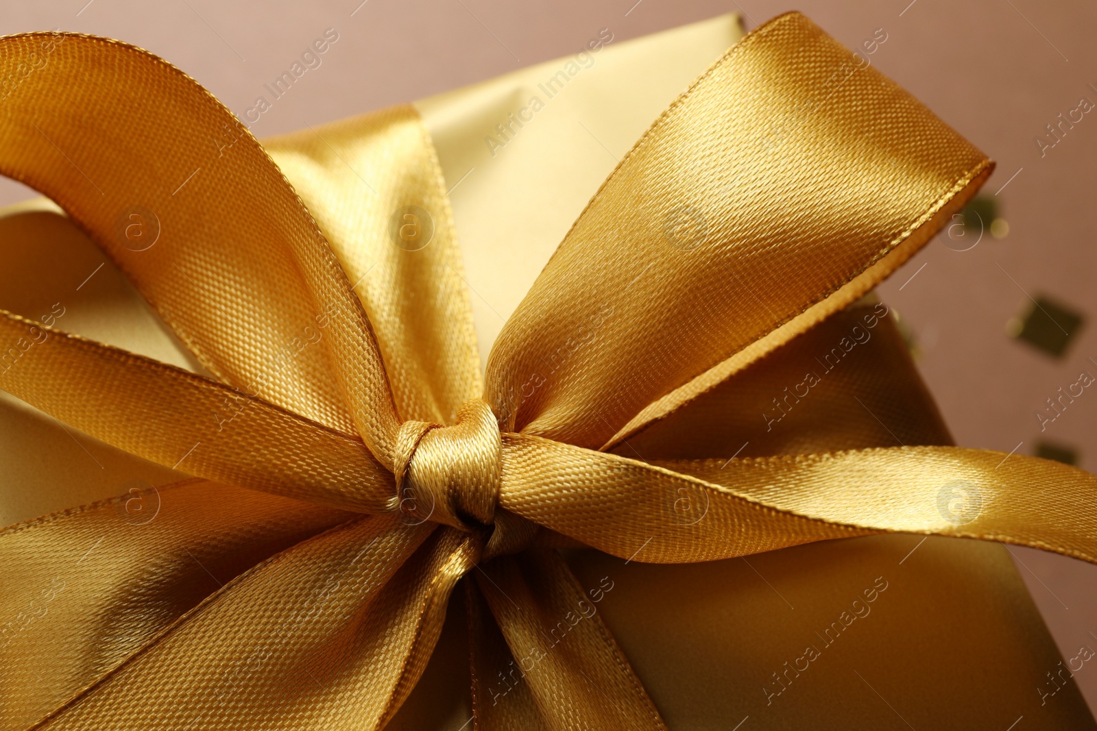 Photo of Beautiful golden gift box with bow on brown background, closeup