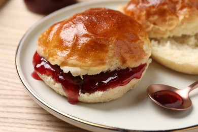 Photo of Freshly baked soda water scones with cranberry jam on wooden table, closeup