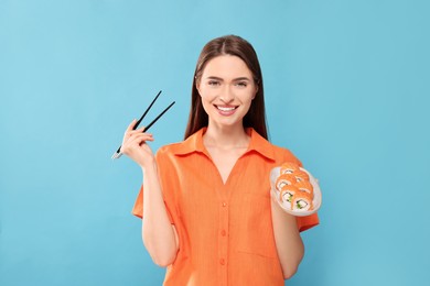 Photo of Happy young woman with plate of sushi rolls and chopsticks on light blue background