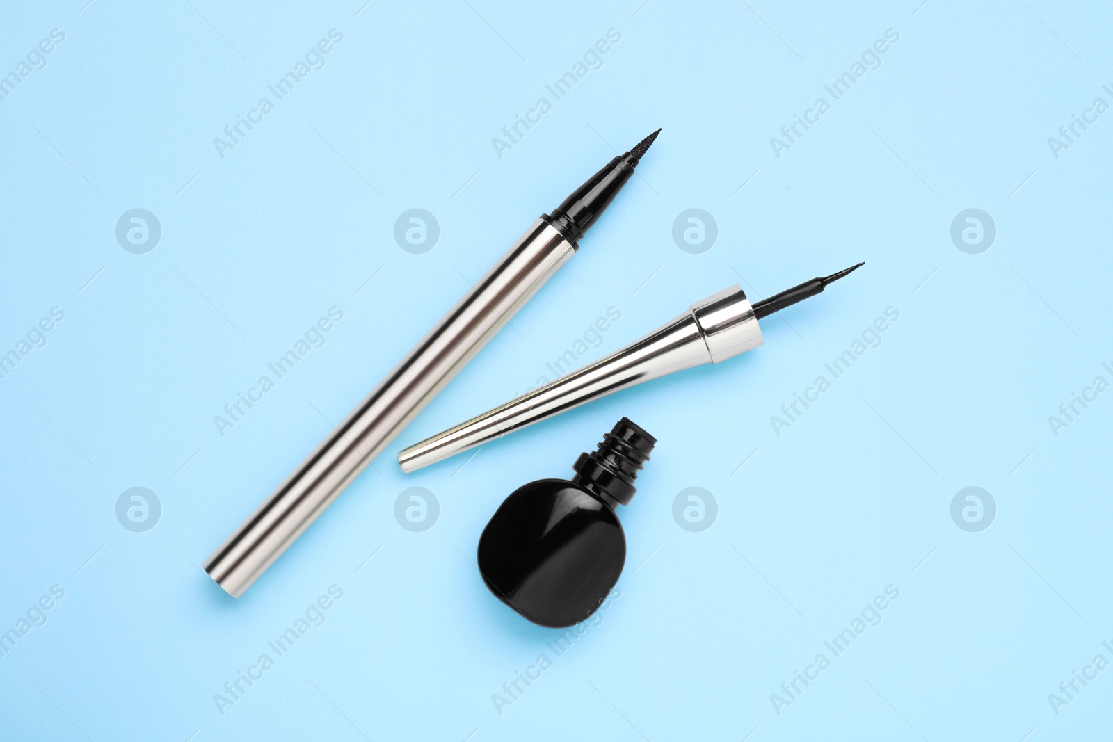 Photo of Black eyeliners on light blue background, top view. Makeup product