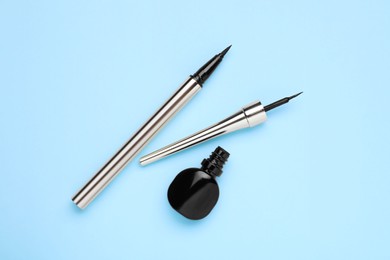 Photo of Black eyeliners on light blue background, top view. Makeup product