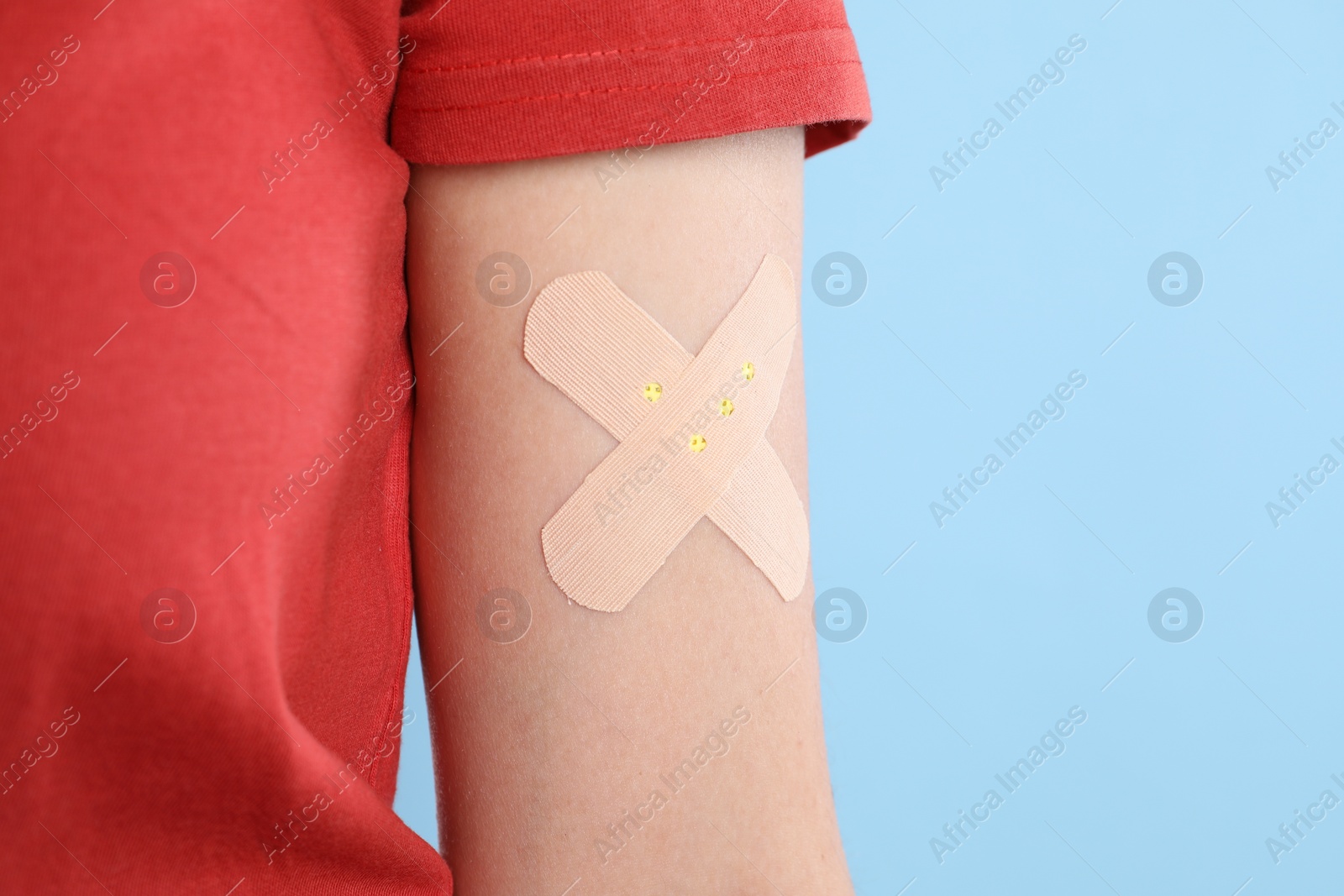 Photo of Woman with sticking plaster on her arm against light blue background, closeup. Space for text