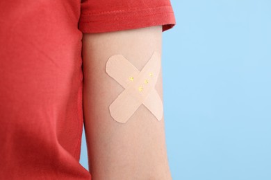 Woman with sticking plaster on her arm against light blue background, closeup. Space for text