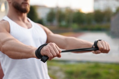 Muscular man doing exercise with elastic resistance band outdoors, closeup