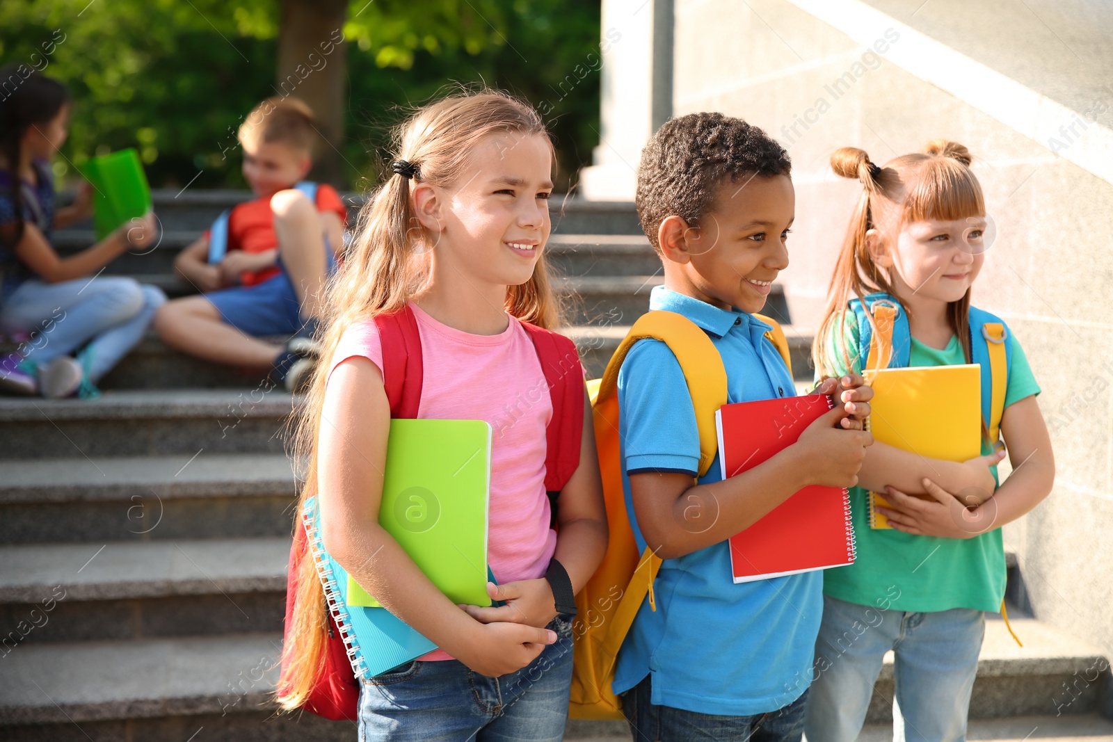 Photo of Cute little children with backpacks and notebooks outdoors. Elementary school