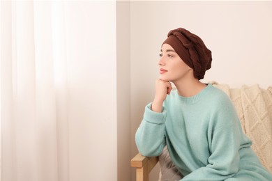 Photo of Cancer patient. Young woman with headscarf near window indoors, space for text