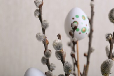 Photo of Beautiful willow branches with painted eggs on light grey background, closeup. Easter decor
