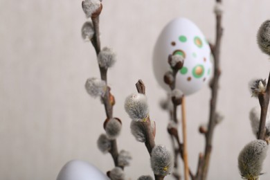 Beautiful willow branches with painted eggs on light grey background, closeup. Easter decor