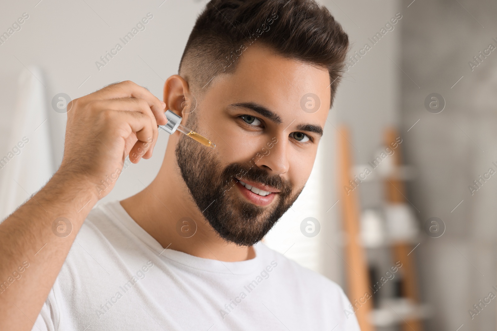 Photo of Handsome man applying cosmetic serum onto his face in bathroom