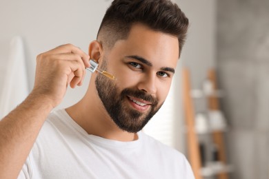 Photo of Handsome man applying cosmetic serum onto his face in bathroom