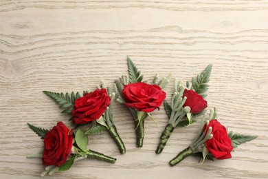 Many stylish red boutonnieres on light wooden table, flat lay