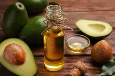 Glass bottle of cooking oil and fresh avocados on wooden table, closeup