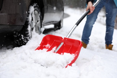 Man cleaning snow with shovel near stuck car outdoors