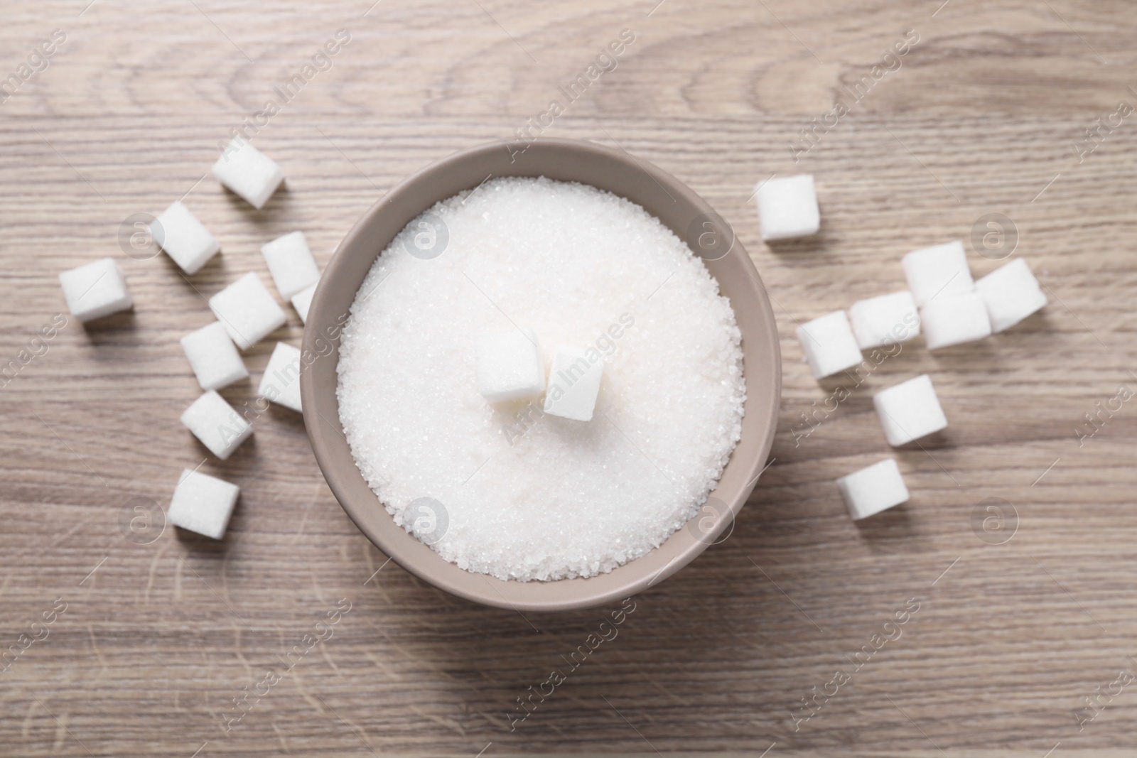 Photo of Different types of white sugar in bowl on wooden table, top view