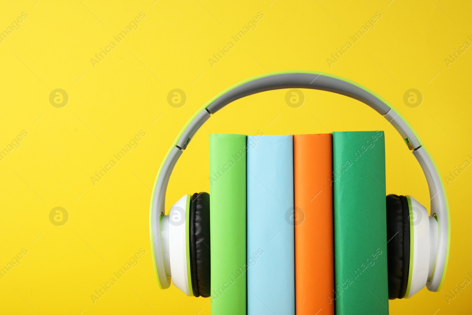 Photo of Books with modern headphones on yellow background. Space for text