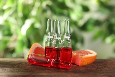 Photo of Pharmaceutical ampoules with medication and grapefruit slices on wooden table, closeup