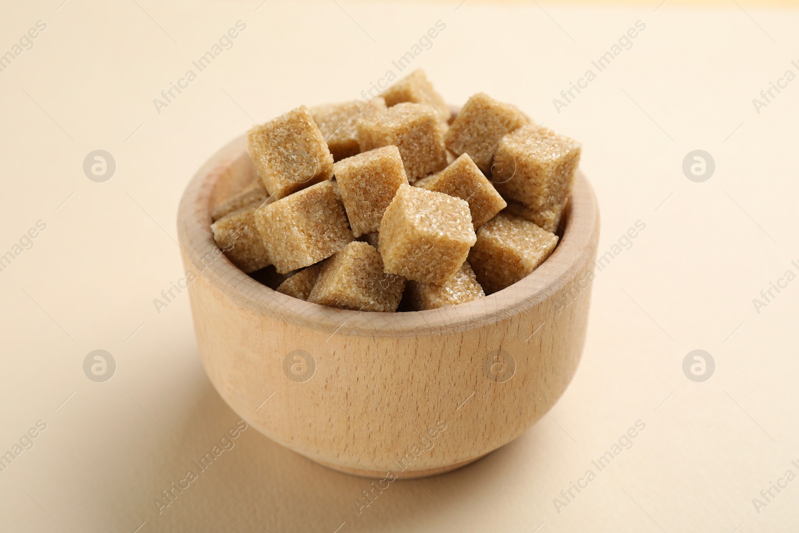 Photo of Brown sugar cubes in bowl on beige background, closeup