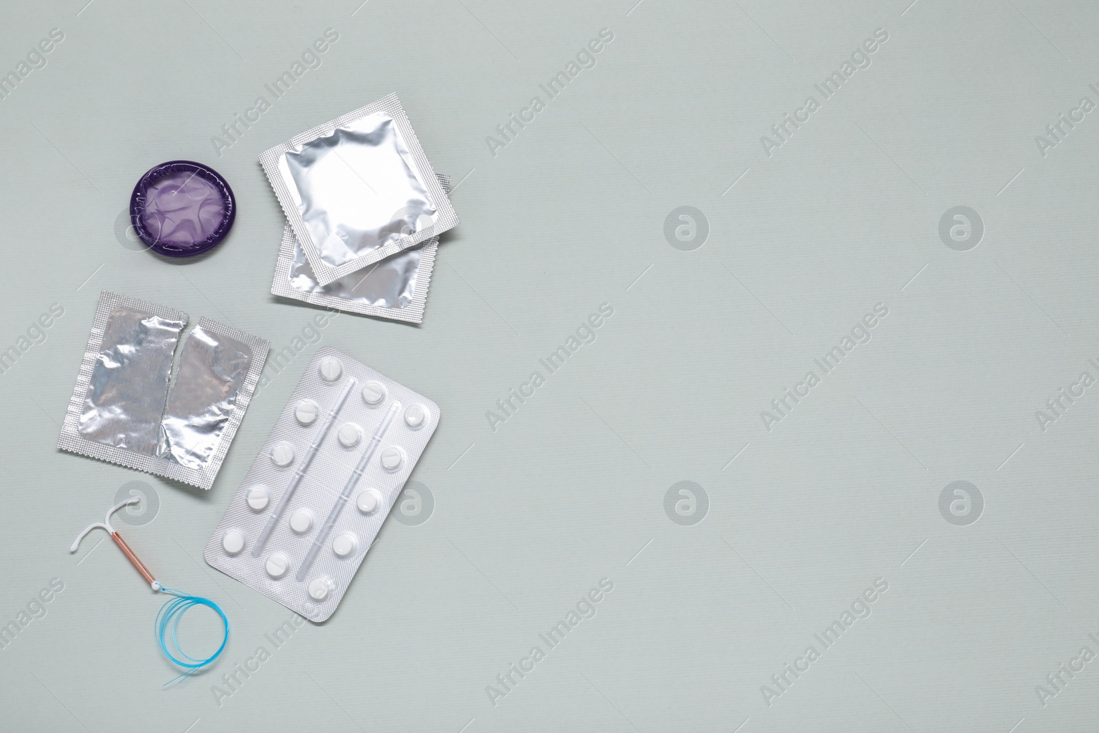 Photo of Contraceptive pills, condoms and intrauterine device on light grey background, flat lay and space for text. Different birth control methods