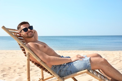 Photo of Young man relaxing in deck chair on sandy beach