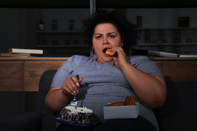 Depressed overweight woman eating sweets in living room at night