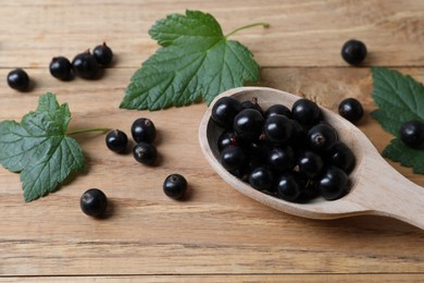Photo of Ripe blackcurrants and leaves on wooden table, closeup