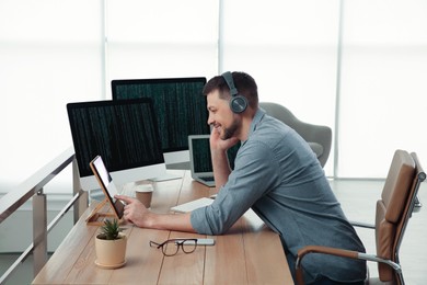 Happy programmer with headphones working at desk in office
