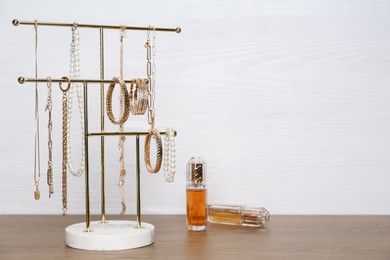 Holder with set of luxurious jewelry and perfumes on wooden table. Space for text