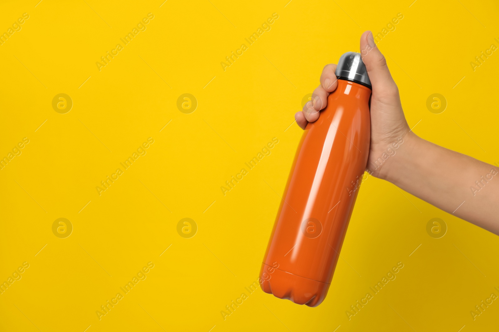 Photo of Woman holding modern orange thermos on yellow background, closeup. Space for text