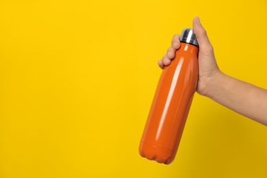 Photo of Woman holding modern orange thermos on yellow background, closeup. Space for text