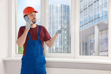 Photo of Professional repairman in uniform talking on phone indoors, space for text