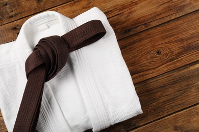 Brown karate belt and white kimono on wooden background, top view