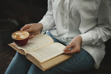 Photo of Woman with cup of coffee reading book indoors, closeup