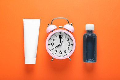 Photo of Container with toothpaste, alarm clock and bottle of mouthwash on orange background, flat lay