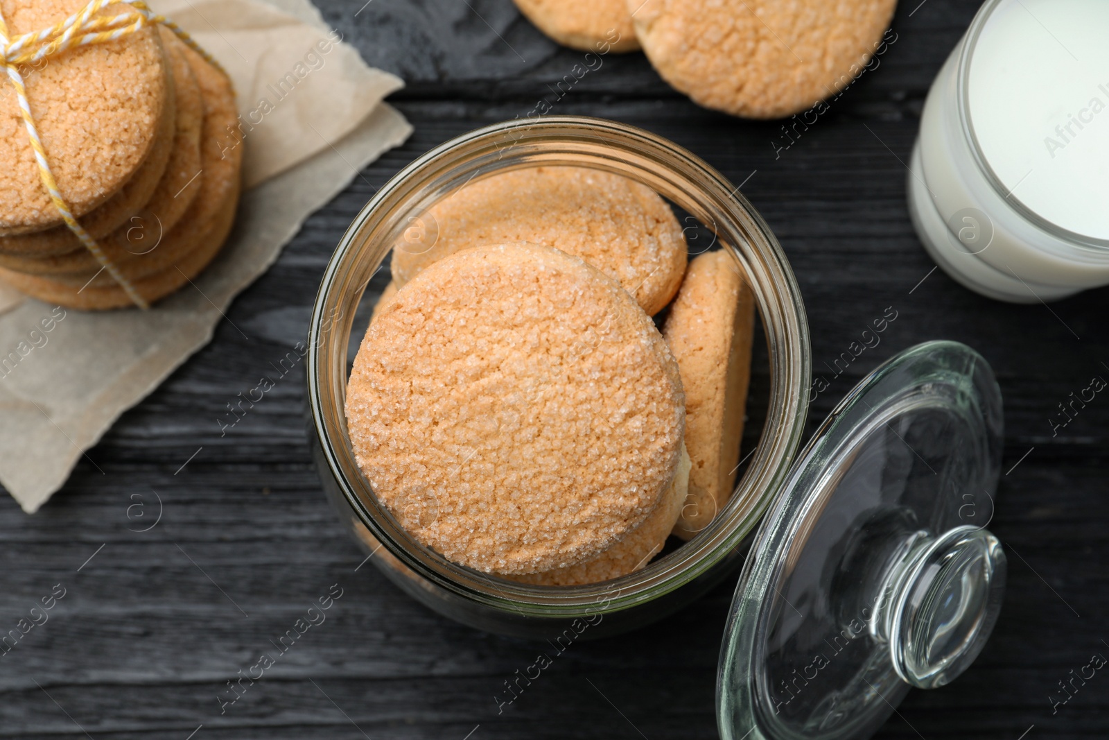 Photo of Delicious sugar cookies and glass of milk on black wooden table, flat lay