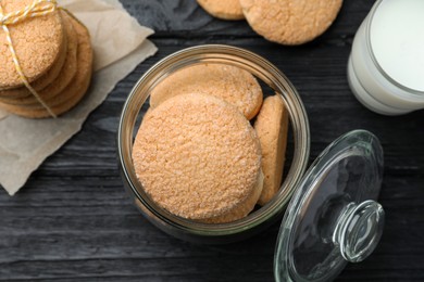 Delicious sugar cookies and glass of milk on black wooden table, flat lay