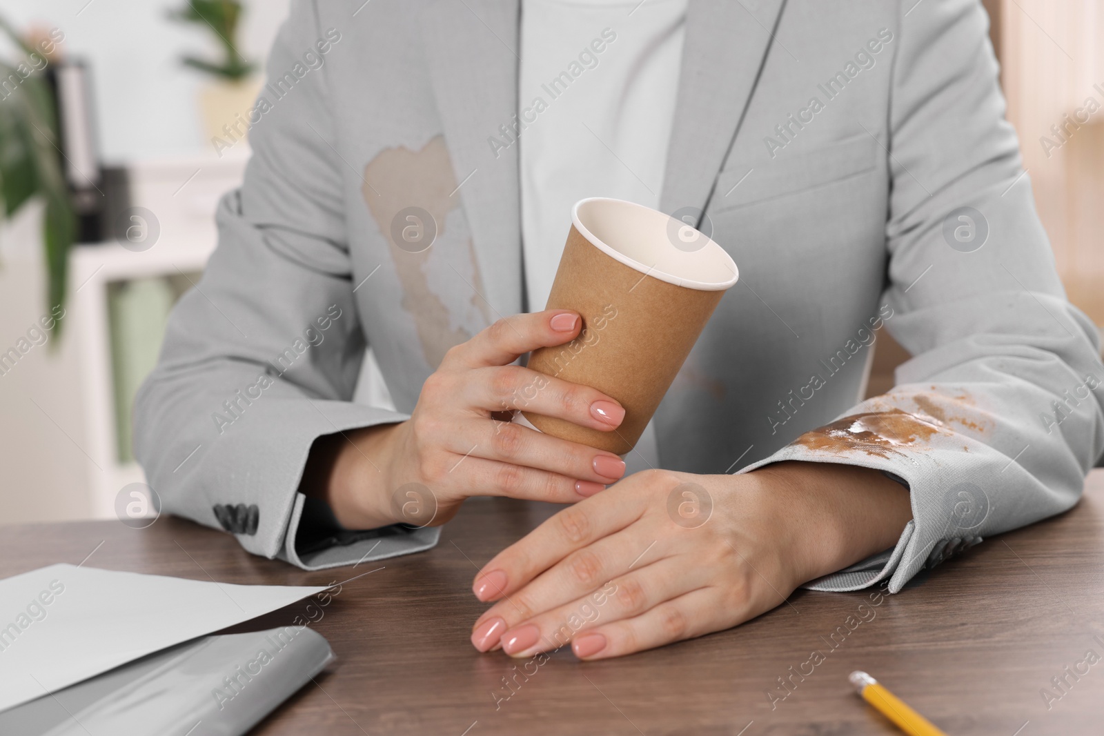 Photo of Woman showing stain from coffee on her jacket at wooden table indoors, closeup