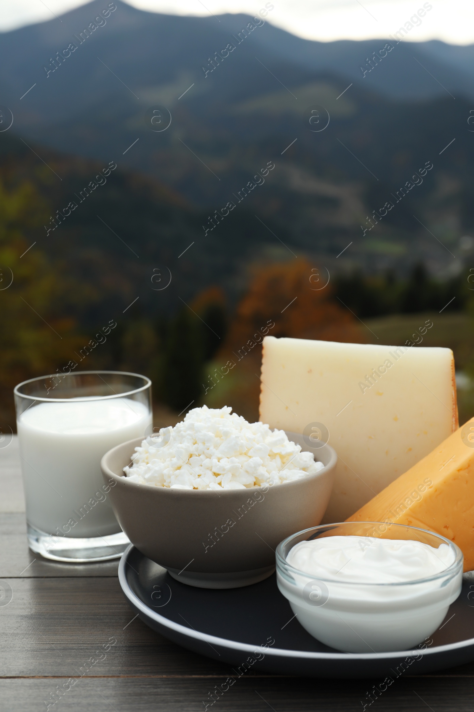 Photo of Tasty cottage cheese and other fresh dairy products on grey wooden table in mountains