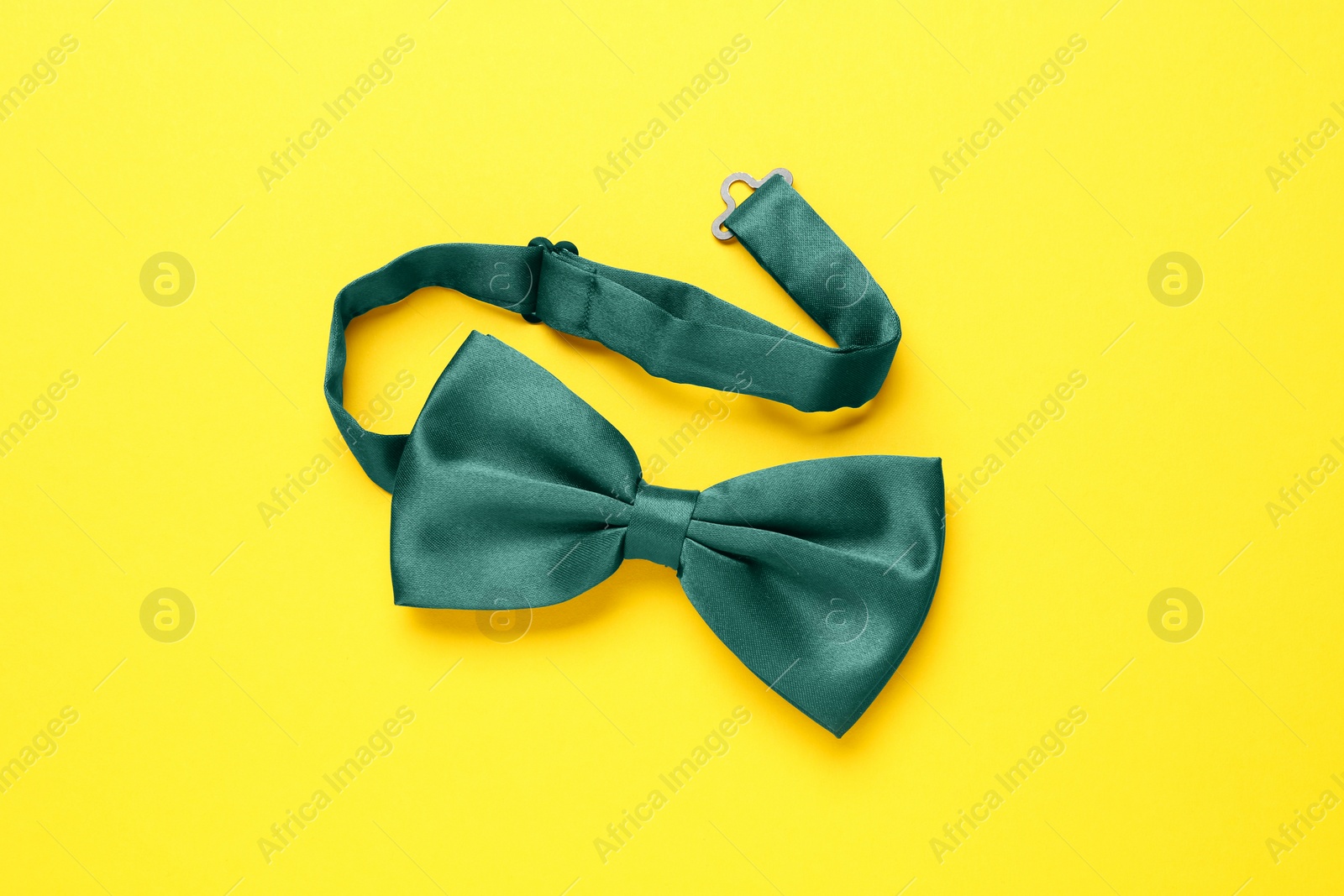 Photo of Stylish green satin bow tie on yellow background, top view