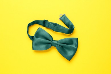 Stylish green satin bow tie on yellow background, top view