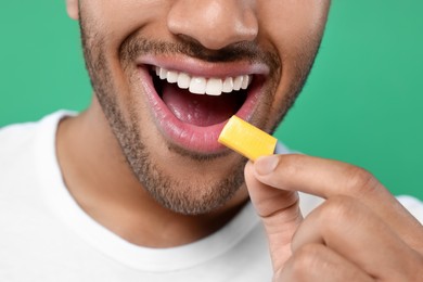 Photo of Happy man putting bubble gum into mouth on green background, closeup