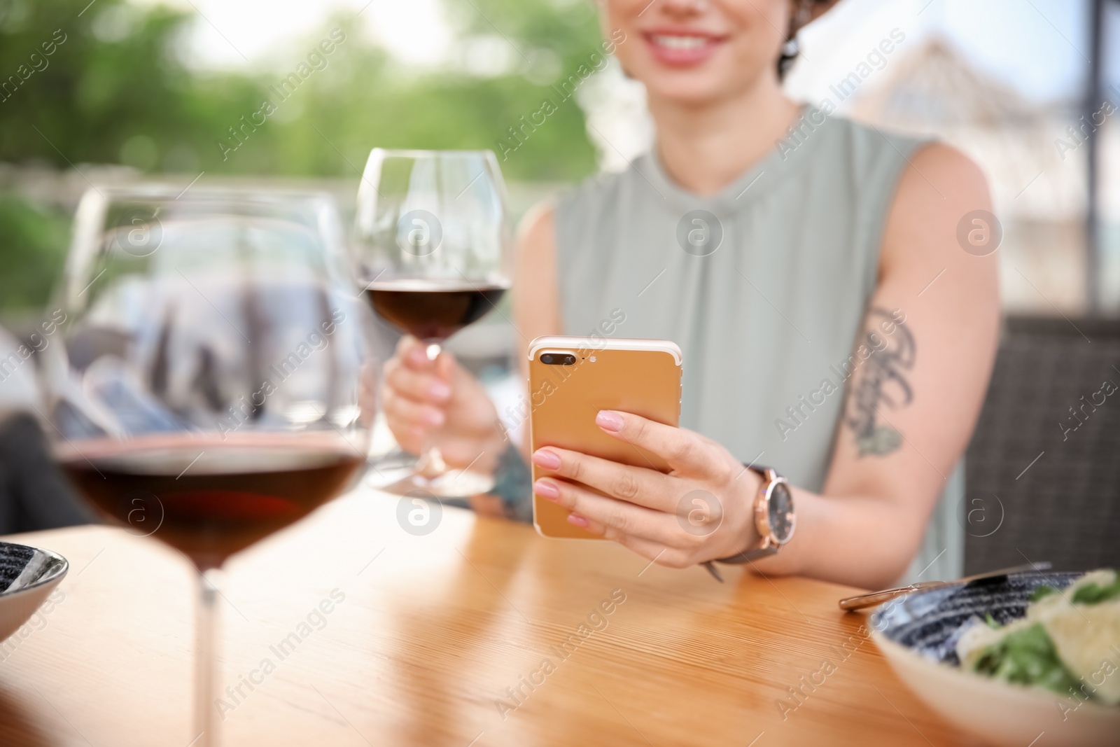 Photo of Young woman with smartphone and glass of wine at table