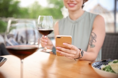 Young woman with smartphone and glass of wine at table