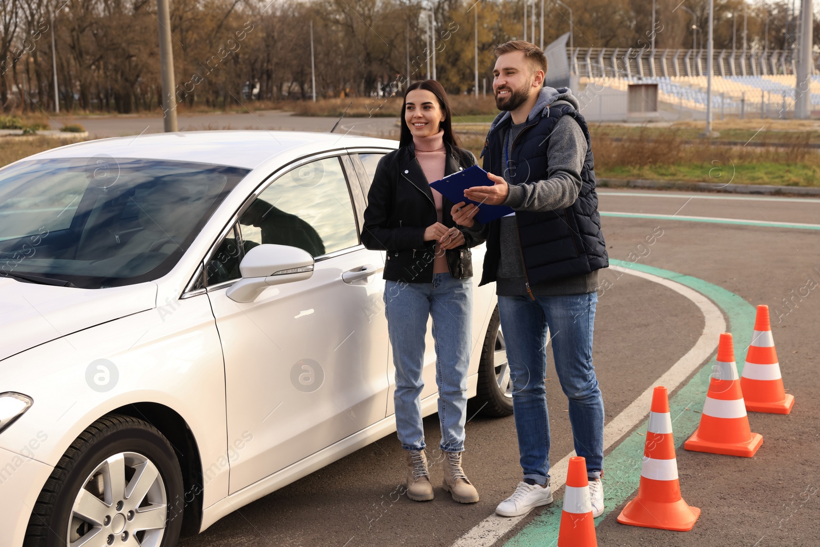 Photo of Young woman with instructor near car at driving school test track